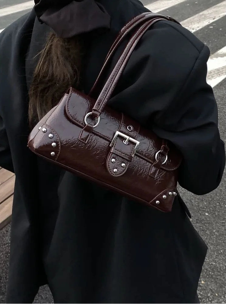 Person holding a brown leather handbag with metal accents on a street.